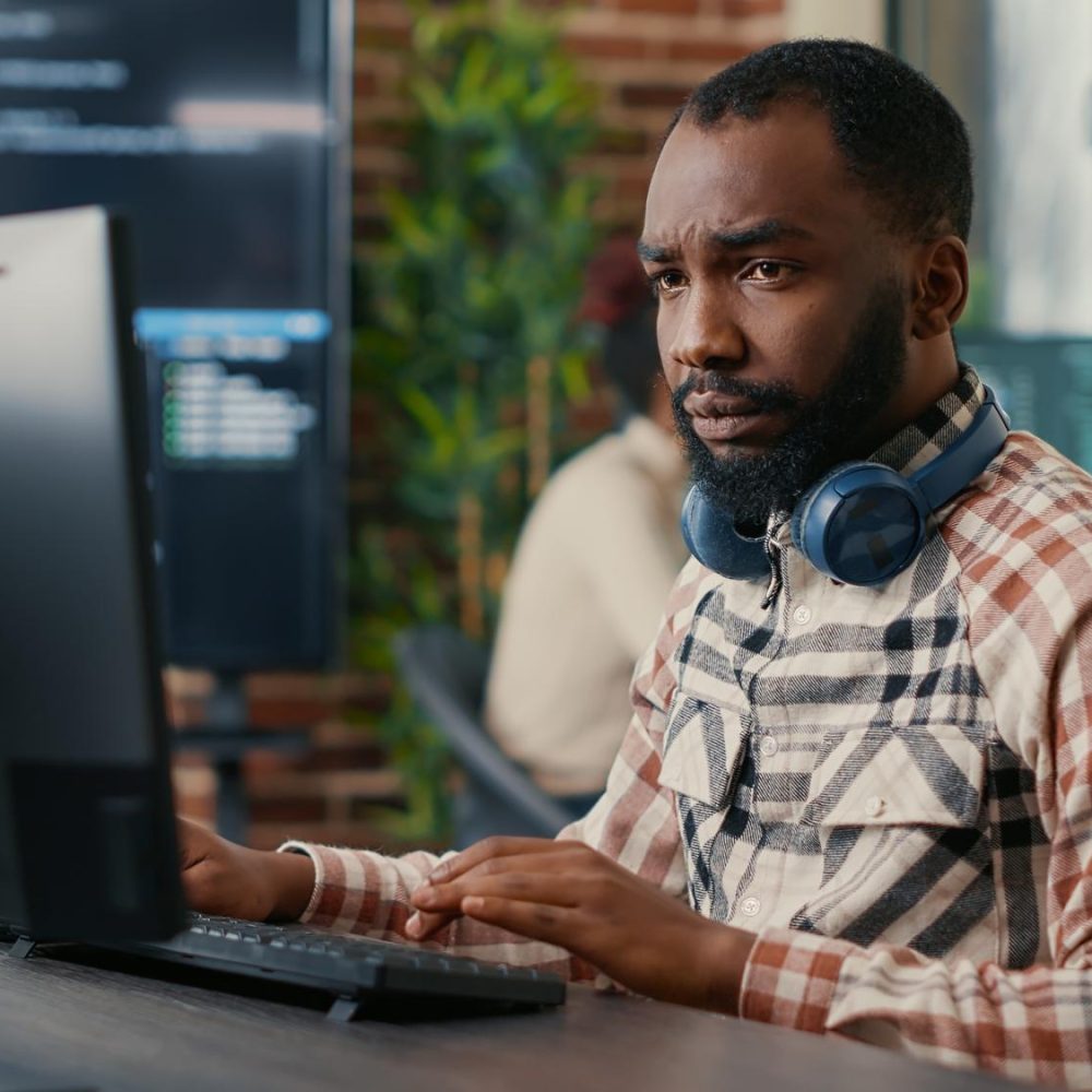portrait-programmeur-afro-americain-concentre-portant-ecouteurs-sans-fil-travaillant-regardant-ecran-ordinateur-tout-tapant-developpeur-logiciels-ecrivant-du-code-dans-bureau-agence-informatique (1)